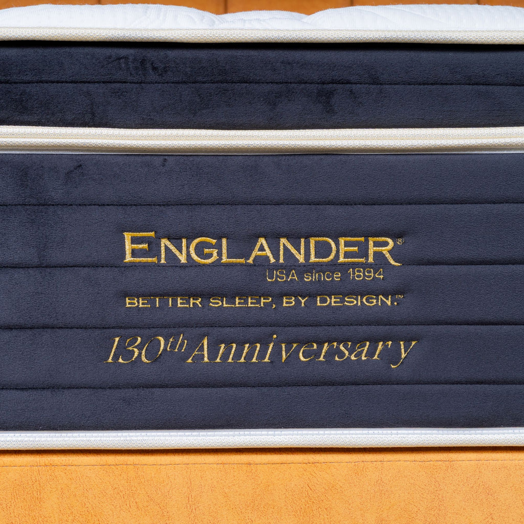 Stack of mattresses with 'Englander' branding and '130th Anniversary' text on a wooden floor.