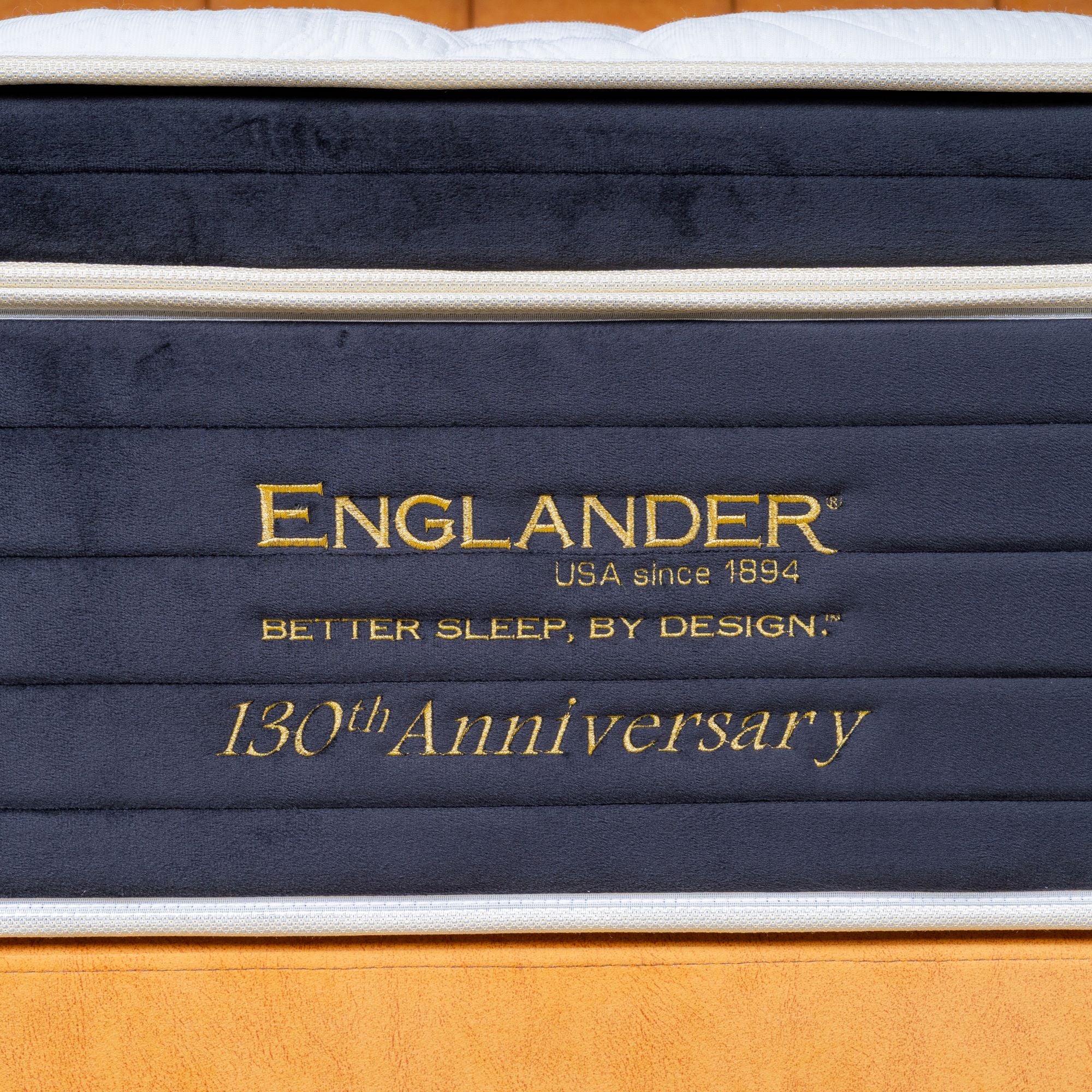 Stack of mattresses with 'Englander' branding and '130th Anniversary' text on a wooden floor.