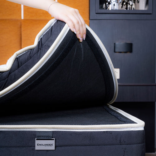 Person opening a navy blue mattress protector with white trim, displaying the brand 'Englander'.